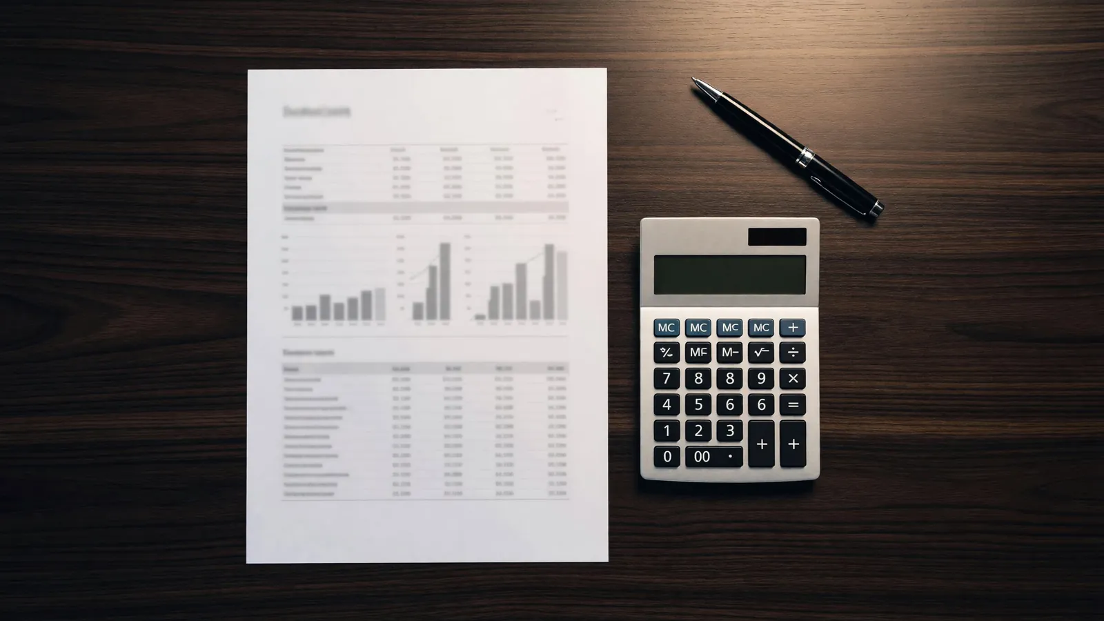 Overhead view of a financial summary with bar charts beside a calculator and pen on a dark walnut desk, comparing what a commercial lease actually costs.